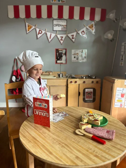 Child dressed as a chef playing in a pretend pizza parlor